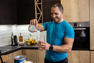 Young muscular guy pouring milk into his shake bowl filled with tasty ingredients, post workout refreshment