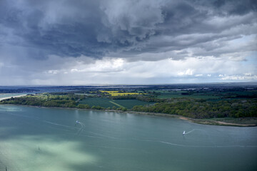 Dark cumulus storm clouds over the West Sussex countryside and estuary near Chichester Marina with sailing boats in the water.