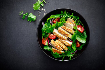 Grilled chicken breast and salad. Fresh vegetable salad with tomato, arugula, spinach and grilled chicken meat in bowl, healthy food, top view. - obrazy, fototapety, plakaty