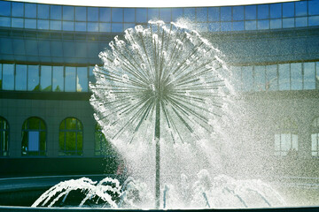 A spherical fountain spewing water under pressure. The fanning structure looks like a dandelion. A hemispherical building with glass windows in the background.