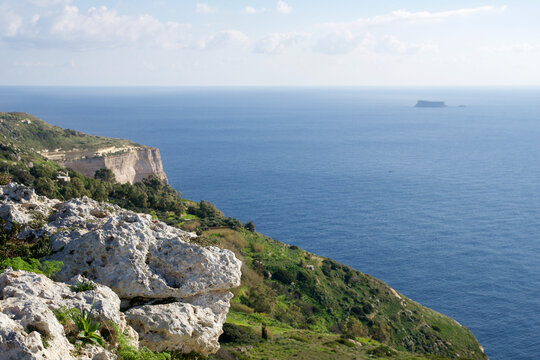 DINGLI CLIFFS, MALTA - JAN 02nd, 2020: Sea coast of Malta with Dingli Cliffs and Fifla Island in the background. Scenic high rising cliffs with panoramic view