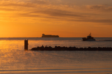 Pilot boat and container ship with seascape in golden morning light and fog.