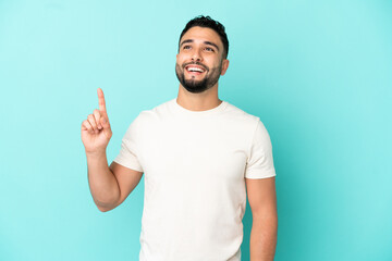 Young arab man isolated on blue background pointing up and surprised