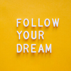 Follow your dream. Motivating and inspiring phrase on bright yellow background. Top view on lifting...