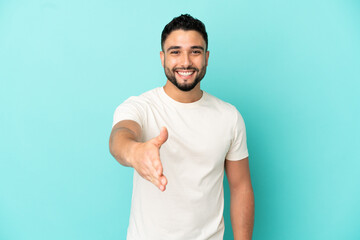 Young arab man isolated on blue background shaking hands for closing a good deal
