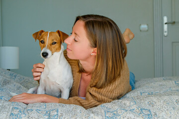 Portrait of young beautiful hipster woman playing with her adorable jack russell terrier puppy on the bed. Loving girl with her dog having fun. Background, close up, copy space