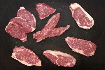 Various Raw Steaks. Sirloin Beef Steaks, Overhead View. Many Raw Striploin Steaks from Marbled Beef on Black Background. Group of Black Angus Beefsteaks. Raw Sirloin Cuts. Uncooked Prime Beef Steaks.