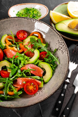 Fresh summer vegetable salad with arugula, tomatoes, bell peppers, avocado and salmon on a plate close up vertical photo