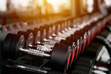 Obraz na płótnie Canvas Rack with many different sizes of dumbbells in the gym. Free weights zone. Sunlight enters the window. Focus blur. Copy space