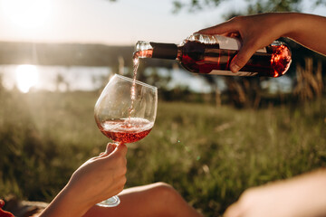 cropped view of couple pouring red wine on meadow, picnic summer day.