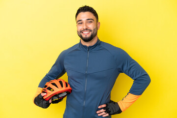 Young cyclist arab man isolated on yellow background posing with arms at hip and smiling
