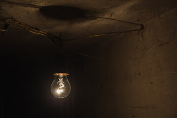 Old tungsten bulb. The incandescent lamp with a tungsten filament wobbles on the wire. Light from a...