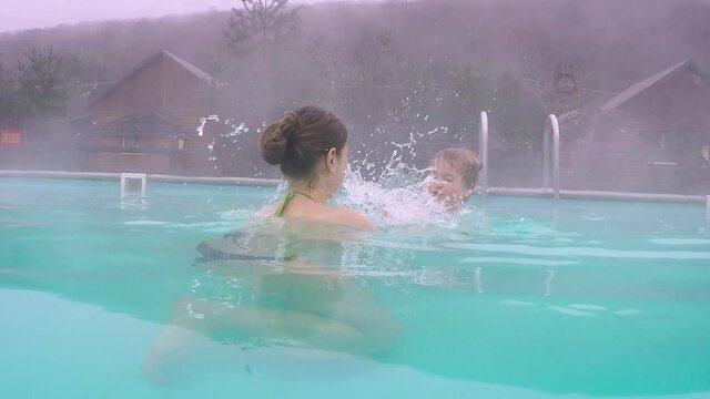Family having fun in geothermal spa resort. Mother and son playing in outdoor hot spring pool in mountains. Offseason travel attraction.