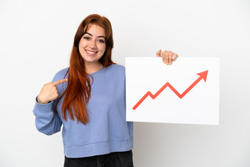 Young redhead woman isolated on white background holding a sign with a growing statistics arrow symbol and  pointing it