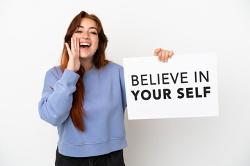 Young redhead woman isolated on white background holding a placard with text Believe In Your Self and shouting