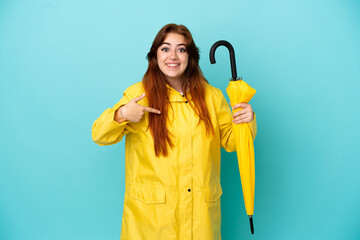 Redhead woman holding an umbrella isolated on blue background with surprise facial expression