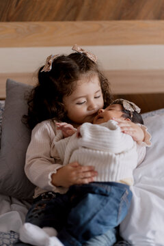Hispanic little girl holding her little sister in bed-Little girl meeting her newborn sister