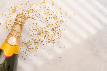 The photo shows a bottle of champagne with a golden neck. Scattered confetti on a white background. White and gold colors. There is a place for your insert no people.