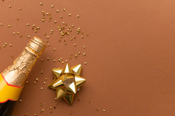 On a beige background, a slice of a bottle of champagne, a New Year's toy, sprinkled with golden confetti. Dark beige background, gold colors. Minimalism. Place for your inscription.