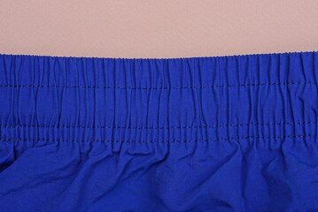 part of blue sweatpants made of crumpled fabric with elastic bands in the belt lies on a pink table
