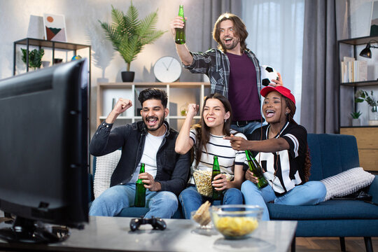 Group Of Four Multiracial Friends Screaming And Gesturing While Watching European Football Championship On TV. Young Fans Emotionally Supporting Favorite Team From Home.