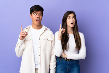 Young couple over isolated purple background thinking an idea pointing the finger up