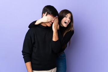 Young couple over isolated purple background covering his eyes to surprise him
