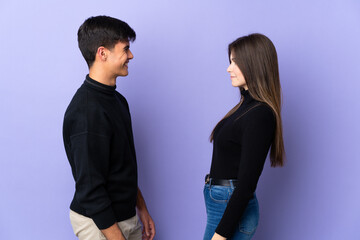 Young couple over isolated purple background looking at each other