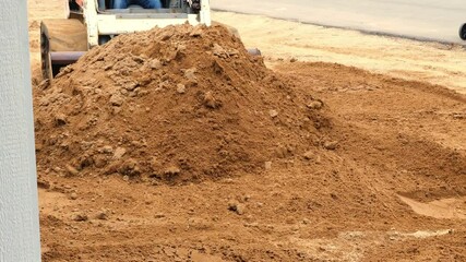 Compact front loader pushes a pile of brown dirt to spread it out, as preparation of the landscape before sod is added, at a construction job site.