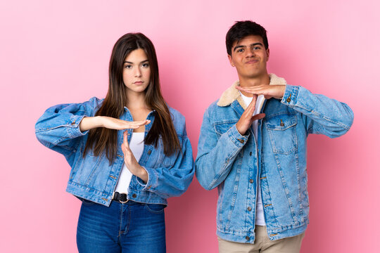 Young couple over isolated pink background making stop gesture with her hand to stop an act
