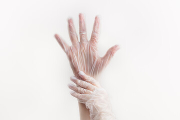 Two female hands wear transparent disposable vinyl gloves above white background. Infection prevention in daily life
