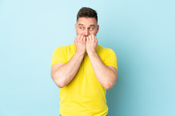 Russian handsome man isolated on blue background nervous and scared putting hands to mouth