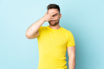 Russian handsome man isolated on blue background covering eyes by hands and smiling