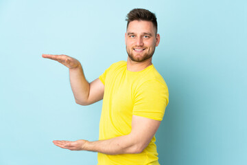 Russian handsome man isolated on blue background holding copyspace to insert an ad