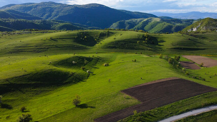 Aerial drone view of green hills and patterned fields on mountain. Beautiful grassy hills at sunset. Meadow and pasture. 