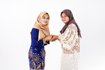 Portrait of lovely Muslim women handshaking ask for forgiveness or apology as Malaysian culture during Hari Raya Aidilfitri or Eid Mubarak celebration, visiting friends and family with white backgroun