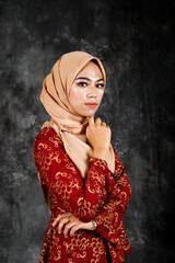 Portraiture of beautiful young Muslim girl wearing hijab and dress known as Baju Kurung Moden. Fashion for dinner, event and feast day. Studio shot with a black oil painting background.
