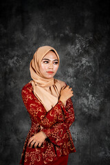 Fototapeta premium Portraiture of beautiful young Muslim girl wearing hijab and dress known as Baju Kurung Moden. Fashion for dinner, event and feast day. Studio shot with a black oil painting background.