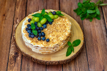Homemade Napoleon cake (Mille-feuille) decorated with grapes, blueberries and mint leaves on a wooden table.