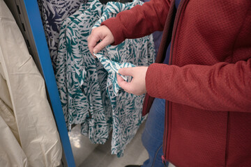 Caucasian woman chooses green shirt with a tropical, white palm tree pattern at a clothing store to buy. The concept of fashion and wardrobe updates. Hands close up shot