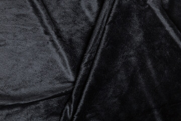 Fototapeta premium Colored black textile satin fabric folded in folds and waves with highlights and texture