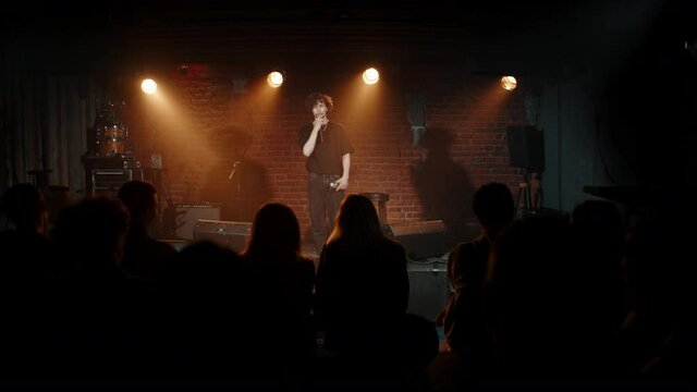 Young Caucasian male comedian performing his stand-up monologue on a stage of a small venue. Shot with ARRI Alexa Mini LF with 2x anamorphic lens