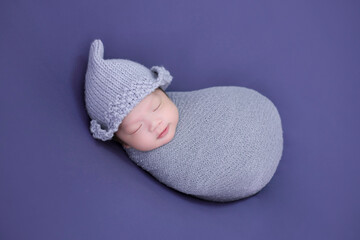 Newborn infant baby sleeping Wrapped in silk And wearing a purple prom silk hat On the foundation cushion In the concept of a newborn child