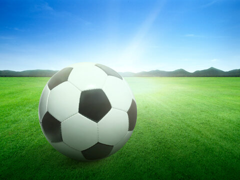 Traditional soccer ball on background image of lush grass field under blue sky