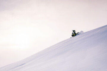 Snowmobile female rider riding on beautiful mountain slope