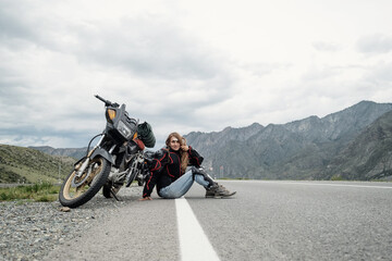 Female rider sitting near her motorcycle on perfect asphalt road in mountains landscape. Long travel in Altai mountain between Russia and Mongolia