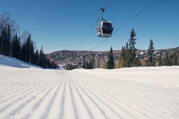 Fototapeta na wymiar Gondola lift in the ski resort on steep slope groomed and prepared for skiing