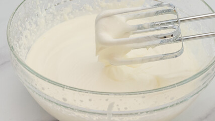 Whipped cream cheese desert recipe. Mixing ingredients in a glass bowl using an electric mixer, close up cooking process, marble background