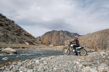 Female motorcyclist seating on Offroad enduro motorcycle in beautiful mountains near the river