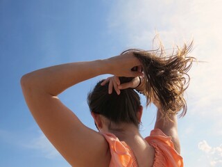 Woman putting her hair into a ponytail on a sunny day - obrazy, fototapety, plakaty